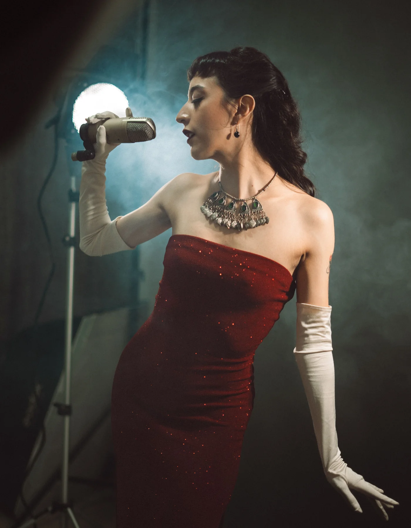 A performer in a sequinned red dress singing into a vintage-style microphone under a spotlight